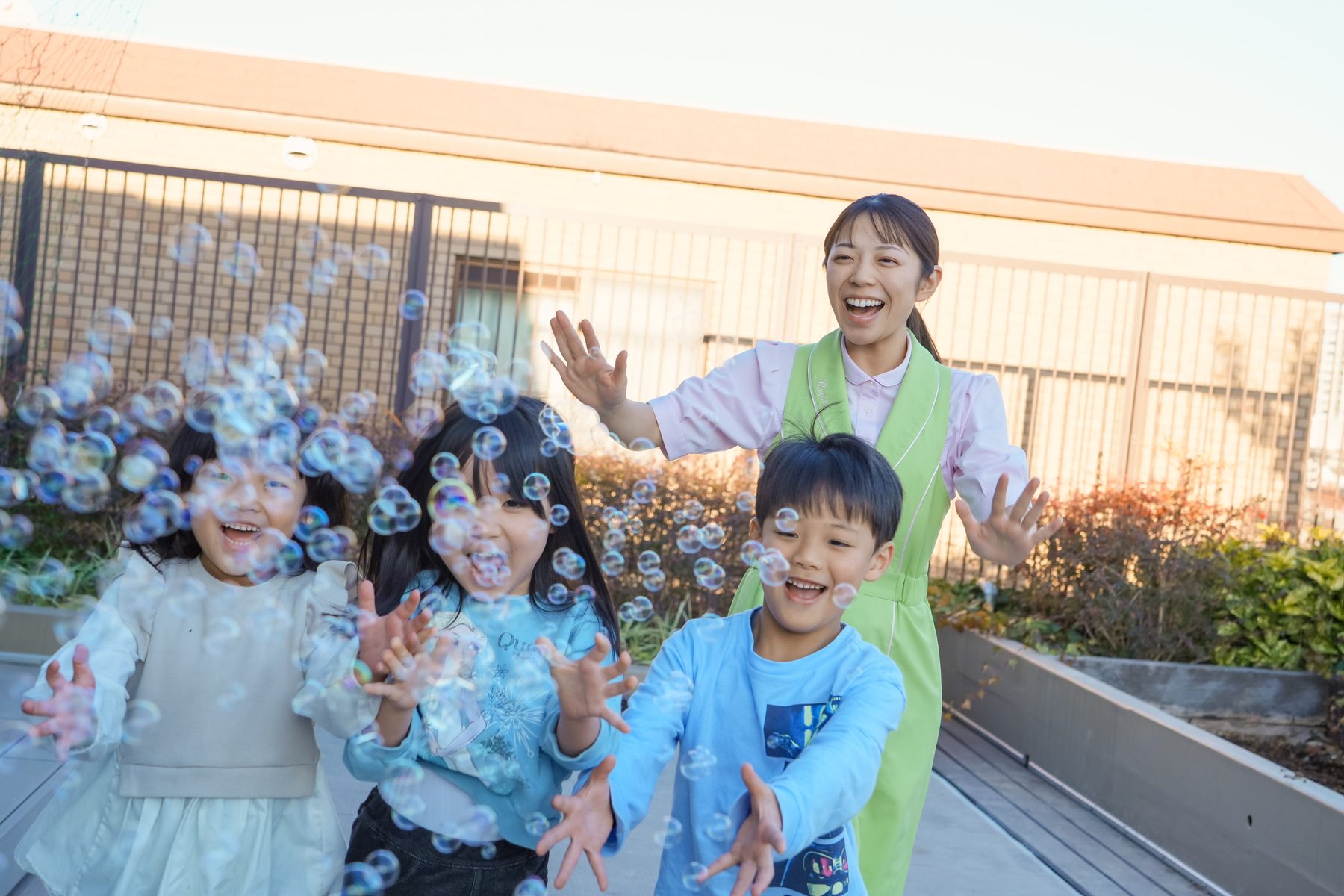 シャボン玉で遊ぶ子どもたちとポピンズの保育スタッフ